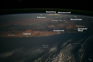 Photo of Earth from the ISS shows the Atlantic Ocean in the foreground with some sporadic cloud coverage. Along the coast is the town of Oranjemund, Lüderitz and the Sand sea. Slightly inland is Springbok/Okiep. Near the end of visible Earth is Gaborone, Rustenberg, Witwatersrand, and Bloemfontein. Each of these settlements appear illuminated by human-made lighting. The Orange river is also illuminated by the peoples who live along the river.