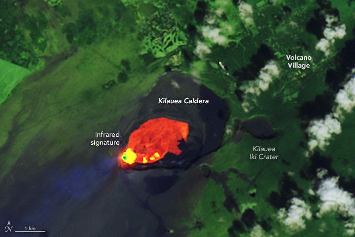 An infrared overlay image of the Kīlauea Caldera and surrounding land. The left edge of the caldera show intense heatin a bright green and yellow, moving away from there to the right the infrared is a cooler orange to red. shows the active lava flow surrounded by previous black hardened flows. The Kīlauea Iki Crater to the right of the larger Caldera is nestled among green landscape with Volcano Village labeled in the upper right.