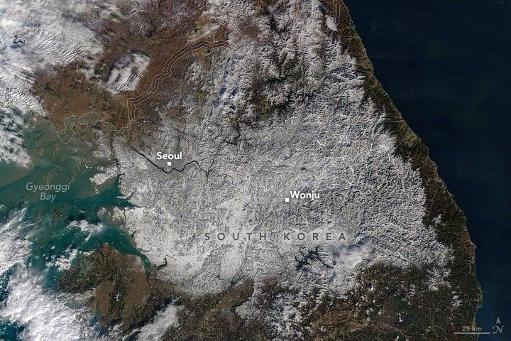 A satellite image of the Korean peninsula shows the land covered in white, highlighting the topography, especially of the eastern portion of the peninsula. Gyeonggi Bay labelled to the left, Seoul is labeled on the upper left of the South Korean section of the peninsula. Wonju is labeled in the center of the snow covered region.