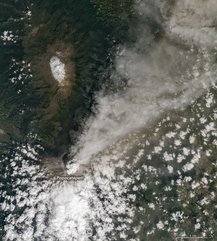 numerous small cumulous clouds can be seen approaching the peak of Popocatépetl from the lower left of the image. At the peak smoke, grayer in color compared to the white clouds, streams conically to the top right of the image.
