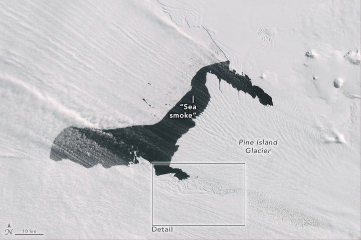A dark pool of sea water interrupts a field of ice on the Pine Island Glacier. Sea smoke can be seen as vapor clouds streaming over the image.