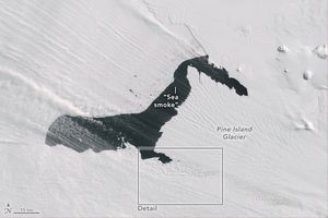 A dark pool of sea water interrupts a field of ice on the Pine Island Glacier. Sea smoke can be seen as vapor clouds streaming over the image.