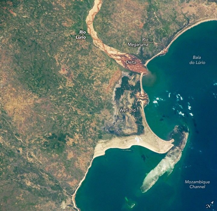 Rio Lúrio curves through the landscape, carving a light beige path that terminates in a weaving delta along the coastline of Baía do Lúrio just above a wetland that stretches to a barrier island.