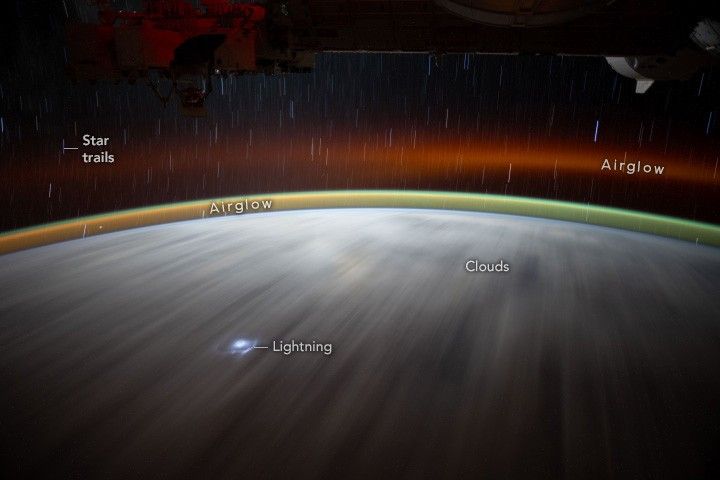 Two layers of Airglow are visible above the Earth's surface, one near the surface and another after a gap of dark space, less bright than the first. Star trails are visible in the dark of space above the Earth's curve.