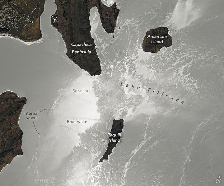 Lake Titicaca in this image appears shades of silver due to the sunglint. Amantani Island is in the upper right, a light brown color, Capachica Peninsula is just left of center at the top of the image. Just below the image center is a long island reaching near the bottom of the image. To the left of that island internal waves are labeled as well as a boat wake on a perpendicular trajector from the island to the main land along the left border.