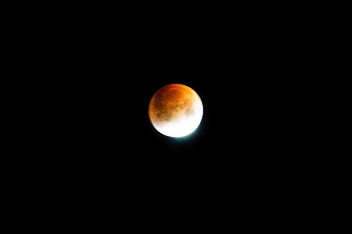 The moon, the upper portion a dark orange to brown hue, the lower lit brightly white.