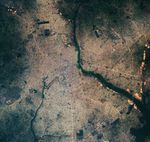 A satellite image centers on Benin City in Nigeria. Networks of neighborhoods, roads, and other development appear gray and span much of the image. Thin arcing strips of green are visible amid the development. These are forested remnants of ancient earthworks built several hundred years ago by the Kingdom of Benin.
