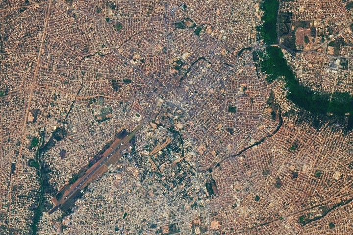 A satellite image centers on Benin City in Nigeria. Networks of neighborhoods, roads, and other development appear gray and span much of the image. Thin arcing strips of green are visible amid the development. These are forested remnants of ancient earthworks built several hundred years ago by the Kingdom of Benin.