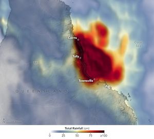 A rainfall data color gradient is overlayed over Queensland Australia. The range of rainfall data spans zero to 100 or more centimeters. The corresponding colors range from light blue to dark red. The coastal region, including the cities of Cairns, Tully, and Townsville are encompassed in a dark red blob of precipitation that mostly precipitated over the Coral Sea to the right.