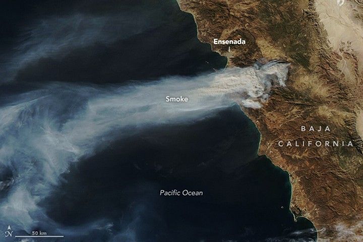 The dark blue of the Pacific Ocean, left, is partially obscured by a stream of smoke emanating from the coastline just South of Ensenada. The smoke moves from opaque to translucent as you increase distance from the origin.