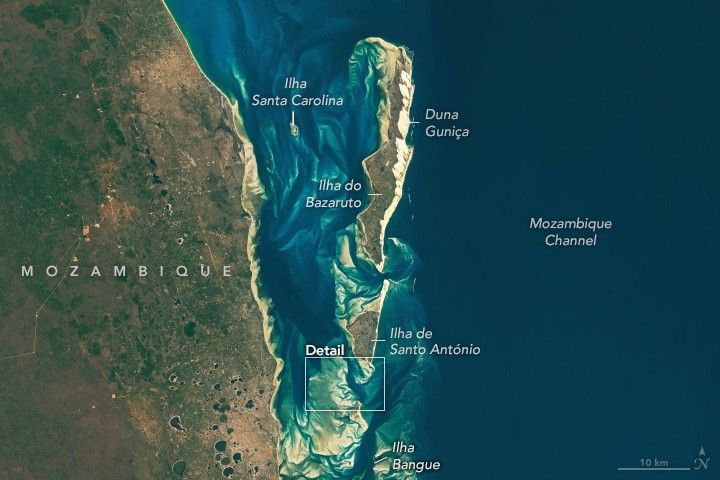 Mozambique, mottled green brown and tan landscape on the left side of the image.  The center of the image features the coastline and the right side the Mozambique Channel. A barrier island  consisting of, from North to South, Duna Guniça, Ilha do Bazaruto, and Ilha de Santo António. At the southern edge the islands are at their closest to the mainland, and there is a wide swath of visible sand deposits in the area.