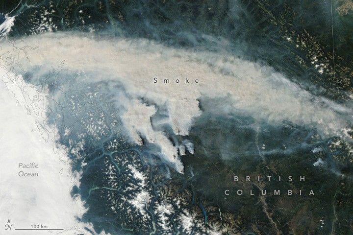 Solid cloud cover obscured the Pacific Ocean, labeled in the lower left corner of the image. Dense smoke obscures the land horizontally from the upper left to the center right in a fairly thick band, but land is visible above and below. There is also smoke emanating from the very center of the image, below the image wide band of smoke.