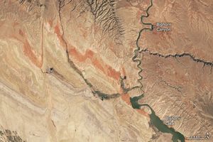 The meandering Bighorn Canyon enters the image at the top center and joins Bighorn lake in the lower right. The landscape surrounding it id beige with reddish strips.