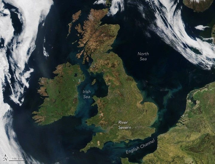 Satellite image of the UK, Ireland, and northern France. The Irish Sea between the two large island countries is labeled and light in color compared to the surrounding deep blue waters. The English Channel at the bottom of the screen is also light in color when compared to the North Sea toward the right of the UK. Clouds swirl over the ocean surrounding the two island nations.