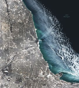 Greater Chicago is shown, left, appearing a translucent pale white color with Lake Michigan, right, also covered near the coast by a sweeping pale white ice layer. The water in the top right is ice free and appears near black, while coastal waters appear lighter and blue-green.