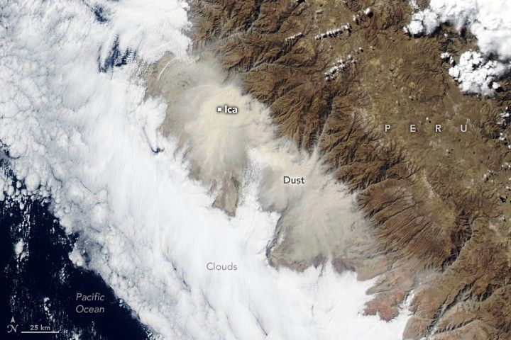 The deep blue of the Pacific Ocean is visible in the lower left corner. A thick layer of clouds and dust running from the upper left to the lower right separate the ocean from the land in the image. The dust is more beige in color than the white clouds and is on the landward side of the image. Ica is labeled, obscured by the cloud of dust. The deep brown mountainous landscape of Peru is visible in the upper right.