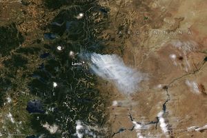Smoke emanates from the Agentina Chile border region, just above Lanin Mountain. This white-gray smoke drift to the bottom right over the arid landscape of Argentina.