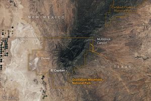 satellite image along the Texas (right) and New Mexico (left) border. An orange border overlay outlines the Guadalupe Mountains National Park in which McKittrick Canyon resides and is in the center of the image. Diagonally down and left on this dark colored mountain range is El Capitan, and to the left of that are light colored smooth formations labeled dunes. In the upper right corner of the image is another orange outline for Carlsbad Caverns National Park.
