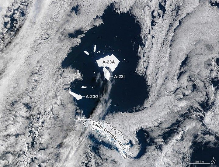 in a gap between clouds icebergs appear north of the coast of South Georgia Island. A-23A is the largest iceberg, A-23I is labeled right next to that, and A-23G is nearer to the island.