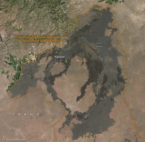 An orange line outlines the Caters of the Moon National Monument and Preserve. Mountainous regions occupy the land up and right of the preserve with some farmed land on the border between it and the mountains.  Lava fields darken the brown landscape in the preserve. Two small arrows point to Kipukas in the upper portion of the preserve.