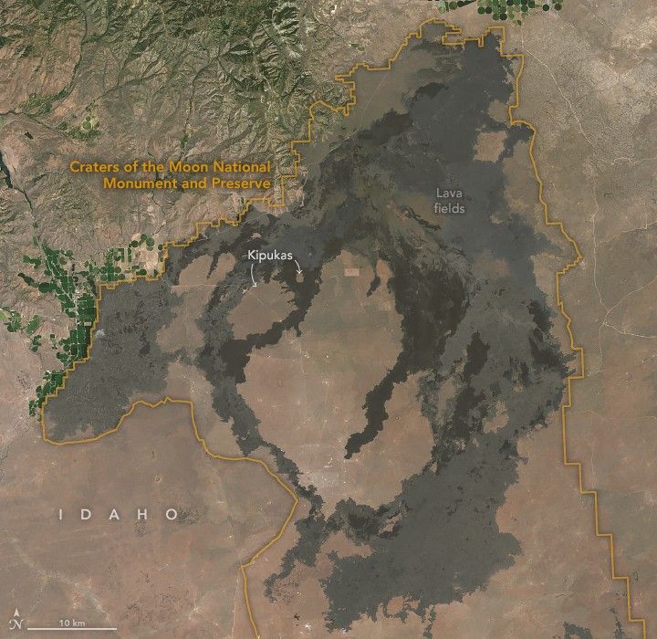 An orange line outlines the Caters of the Moon National Monument and Preserve. Mountainous regions occupy the land up and right of the preserve with some farmed land on the border between it and the mountains.  Lava fields darken the brown landscape in the preserve. Two small arrows point to Kipukas in the upper portion of the preserve.