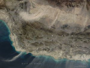 Multiple plumes of dust stretch out over the Gulf of Oman at bottom of the image from Iran and the Hamun-e Jazmurian occupying the top of the image. It is a stretch of land that seems relatively flat and without vegetation. lighter in color than the surrounding region.