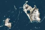 A satellite image shows two rocky islands partially covered in snow and ice in the South Atlantic Ocean. Some ice clings to the shore of the larger island on the right side of the image, and some drifts in the dark blue water.