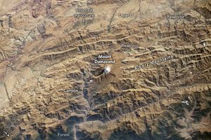 The tan landscape is covered with significantly mountainous terrain which shades the side of each peak that is nearer to the bottom of the image. At the very bottom these shadows give way to green coloration from Forestation. Snow peaked Mount Damavand centers the image as part of the Alborz Mountains. A canyon runs veritcally alongside, to the left of Mount Damavand. A Reservoir sits just up and to the right of the mountain. Another reservoir is labeled in the top right in a relatively flat desert valley. The leftmost section of the valley is sparsely interrupted by a green-brown color labeled irrigated agriculture.