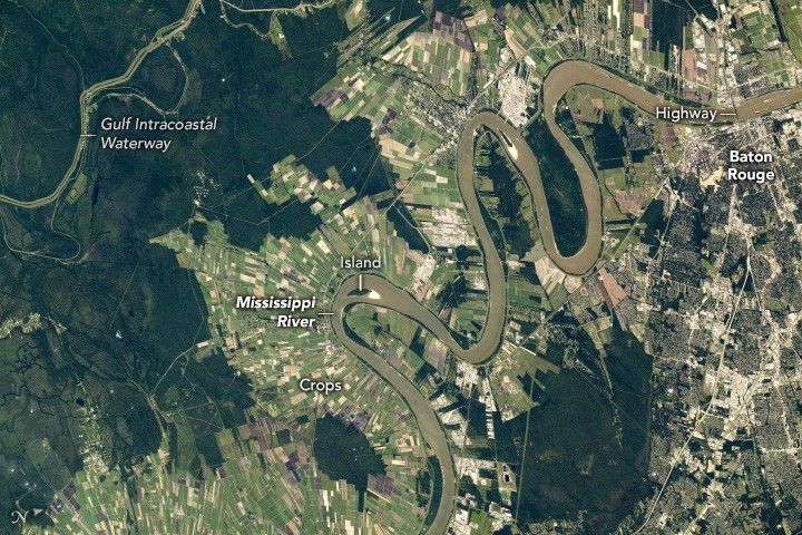 farm fields radiate away from the meandering Mississippi River. Dark green foliage fills the upper left with the Gulf Intercoastal Waterway cutting through. The right edge of the image includes the built up area of Baton Rouge.