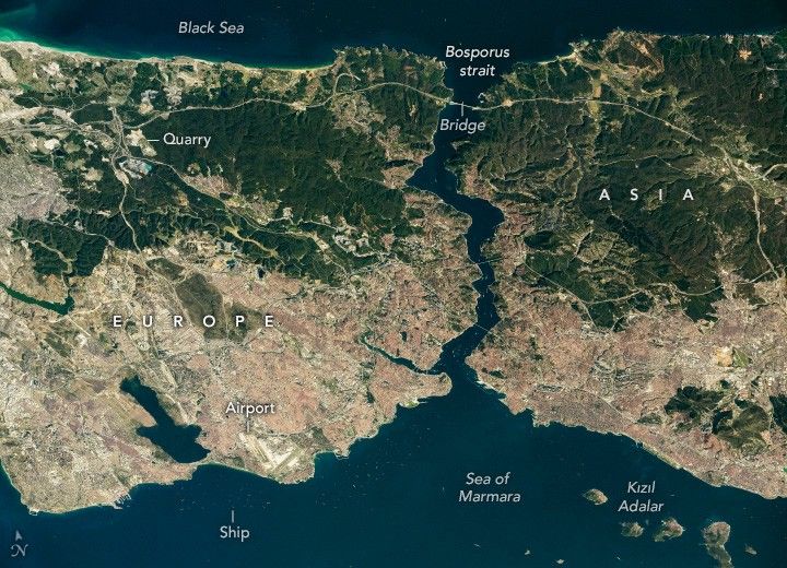 The Black Sea frames in the top of the image with it's dark waters. The Bosporus strait connects it to the slightly less dark blue Sea of Marmara at the bottom of the image. On either side of the strait are landmasses, Europe is labeled left and Asia right. Both landmasses have more forested region in the northern latitudes and more human settlement on the lower coast.