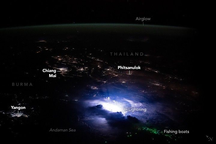 In the foreground, bright flashes of lightning from a thunderstorm loom near fishing boats offshore of Burma’s largest city, Yangon.  The boats are visible as speckles of pale greenish lights in the Andaman Sea. This view from the space station looks across a populated region where the countries of Burma (Myanmar), Thailand, and Laos share borders. The city lights, particularly of Chiang Mai, are visible in the middle left, and Phitsanulok just right of center. At the top of the image is Airglow, a gently arcing faint glow over the Earth.