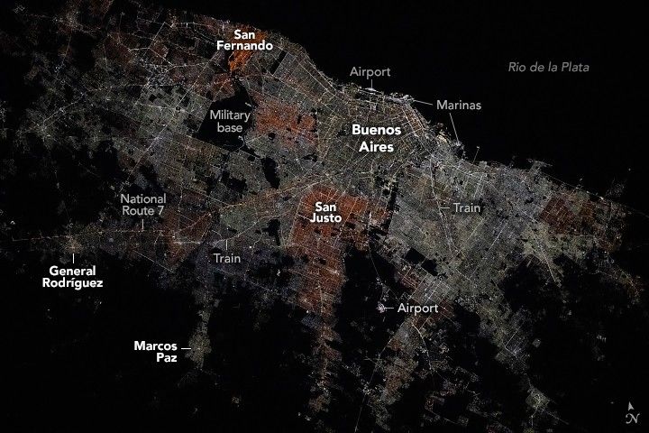 The Buenos Aires streets glow with light from human activity. Train lines, major roadways and the airports are all distinctly visible and labeled. The lights fade the farther inland you look at the image with a completely dark Rio de la Plata occupying the upper right portion of the image. One distinct dark swath within the illuminated streets of greater Buenos Aires is a Military base. San Fernando in the upper left and San Justo, southwest of Buenos Aires, appear to have more auburn colored lights than the rest of the image.