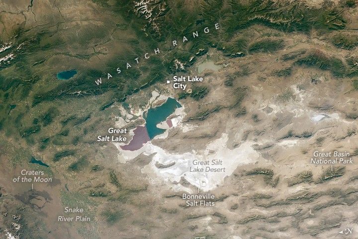 The Wasatch Range of mountains, covered in a deep green that becomes gradually more sage as it blends with the beige valleys below, span horizontally across the top of the image. Below that is Salt Lake City, nestled just above the Great Salt Lake. Below that is the Great Salt Lake Desert, which includes the Bonneville Salt Flats, all of which is white to off white. To the right is Great Basin National Park amid the gray brown dusty landscape. In the lower left are the Craters of the Moon and the Snake River Plain. The landscape in this portion of the image appears more true brown than the gray-brown of the lower right.