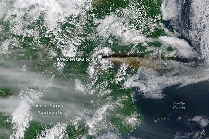 A dark brown to gray plume of smoke emanates from Klyuchevskaya Sopka at the center of this image on the Kamchatka Peninsula. The plume streams due East toward the Pacific Ocean, visible, but partially obstructed by clouds along the right side of the image.