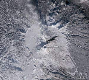 a snow covered volcano peak has an interior ring of smooth snow labeled the caldera rim, a dark streak labeled lava to the upper left and the craggy peaks and valleys of the Kamchatka peninsula surrounding.