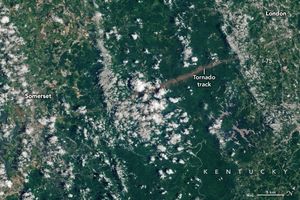 The towns of Somerset, left, and London, right,  in Kentucky are divided by a large swath of deep green foliage. Between the two towns a line of brown land disrupts the foliage and is labeled as a tornado track. Sporadic cloud cover covers much of the image, and the two towns show varied forms of land use including farmed fields in tan shades.