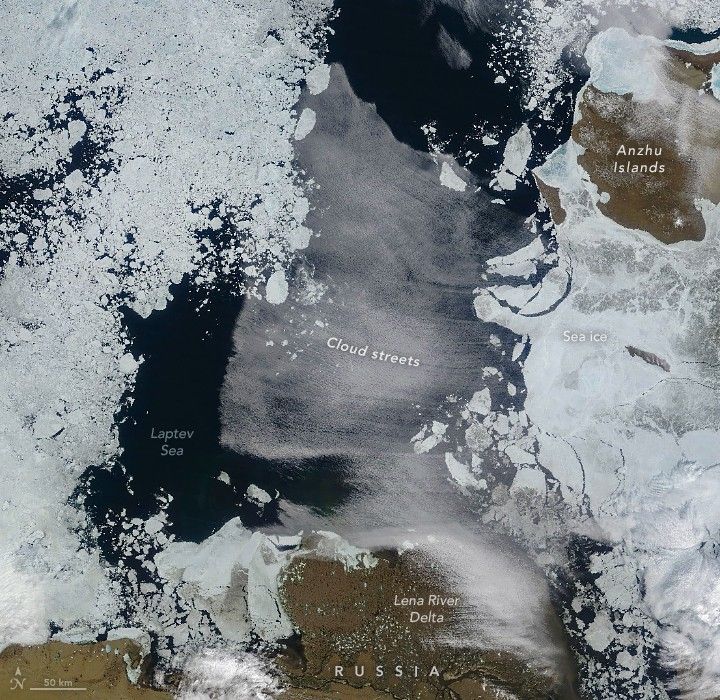 Thins streams of clouds horizontally streak across the deeply dark blue Laptev Sea. Icebergs occupy the left edge of the image and partially broken sea ice the right side. At the top right the Anzhu island disrupts the ice with it's brown color. The brown land of frozen Russia frames in the bottom of the image, the Lena River Delta is at the bottom center.