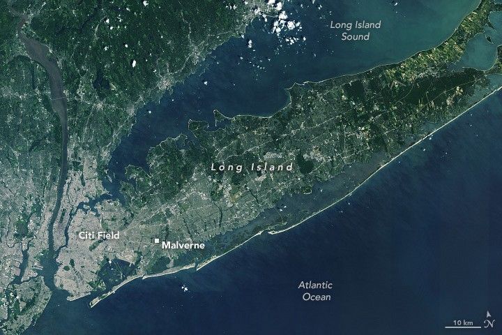 Long island centers in the image, the deep blue Atlantic Ocean below, and the Long island sound, lighter in shade, above. Citi Field is marked on the far left of Long Island and Malverne slightly further right of that. Scanning across the image left to right the island goes from densely settled and gray in color to gradually more green.