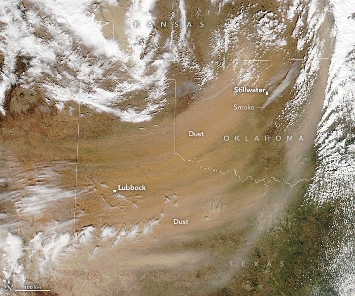 satellite view of Texas, Oklahoma, and Kansas with state lines overlaid on the landscape show sweeping light orange haze of dust encompassing Lubbock Texas and sweeping up and to the right over Stillwater Oklahoma. Multiple streams of smoke emanate from the region around Stillwater and show light gray drifting toward the top right corner of the image. White clouds populate most of the top left corner and the very edge of the upper right.
