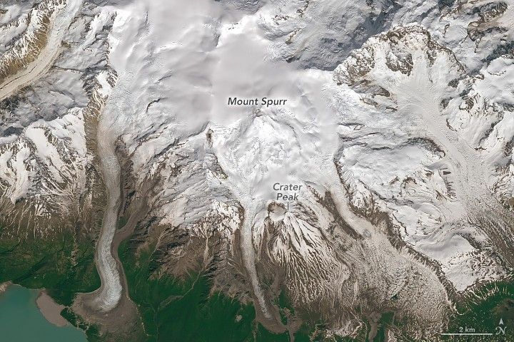 Snow covered mountainous terrain, Mount Spurr label is centarlly located in the image. Crater peak is lower and slightly right of that and is where the brown land starts to peak through the snow in streaks. In the lower left corner there appears to be a body of blue-green water.