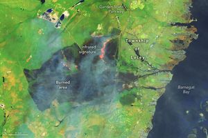A large dark burned area with a bright orange infrared signature resides left of the Township of Lacey, a coastal settlement nestled between the Garden State Parkway and Barnegat Bay on the right edge of the image. The land is bright green in color where not burned.