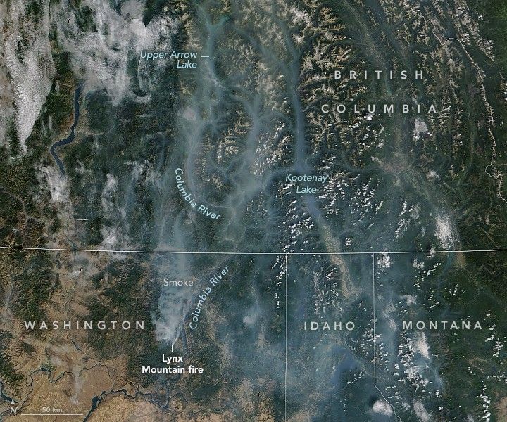 the Pacific Northwest along the U.S. Canada Border. The national and state borders are overlayed on the landscape and labeled. Smoke Emanates from the Lynx Mountain fire in Washinton near the Colombia River. The smoke streams north and is most dense in river valleys. Smoke obscures Upper Arrow and Kootenay Lake in British Colombia.