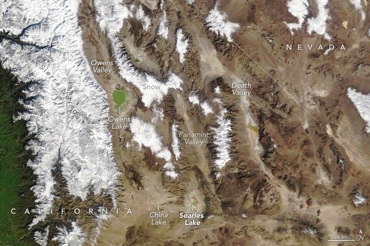 The Snow covered Sierra Nevada peaks frame in the left side of the image. To the right are a series of valleys and additional snow covered peaks. Owens Valley and Owens lake border the Sierra Nevada. At the bottom of the image and further right Are the China and Searles Lake. Searles Lake, despite very similar color to the surrounding brown terrain bears water. The valley to the right of Searles is Panamint Valley, which also holds some water in this image, though only a tiny amount. The next valley over is Death Valley, also bearing water in this photo, and just on the California side of the border with Nevada, included as an overlay in this image.