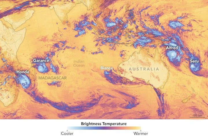 A brightness temperature gradient overlay brightens cold spots and cloud to a blue white, while warmer areas of the map are orange to yellow. The image features centers the Indian Ocean near the West Australian coast. To major storms, Honde and Garance are seen at either end of Madagascar. A smaller storm is near the West coast of Australia. Off the northeastern coast of Australia two storms, Alfred and Seru. All of these storms are bright blue and have extended tails of darker blue sweeping from them.