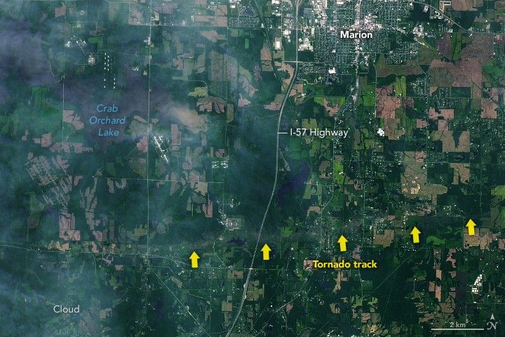 South of the city of Marion, seen top just right of center as a region with gridded roadways and more dense building coverage, is a discolored streak across the landscape labeled tornado track. This area appears to be covered in deep green foliage and paler farmed fields. The track is near perpendicular to Highway I-57 that runs through the image vertically. A dark region on the landscape in the upper left is labeled Crab Orchard Lake.