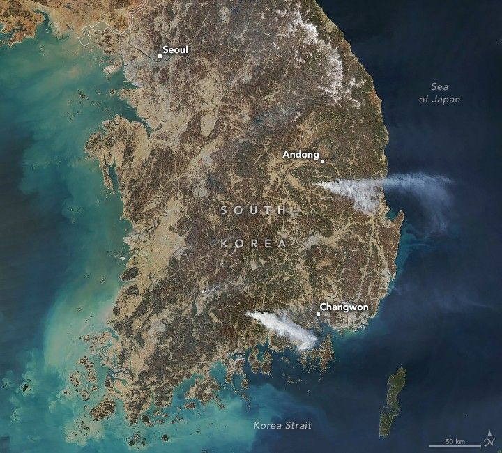 The Korean peninsula is shown, dark waters of the sea of Japan to the right, blue green of the Korea strait mixes directly under the peninsula and left of Korea. Korea appears brown in color, with distinct regions of increased elevation appearing darker. Changwon is a labeled town on the lower coast on the right. A steam of smoke emanates directly left of Changwon. Seoul resides in the top left corner and Andong in the center right of the country. Another stream of smoke emanates directly below Andong.