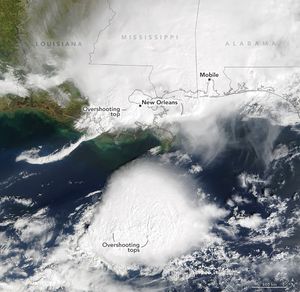 Image of the Gulf and gulf coast from Louisiana to the Florida Panhandle. Cloud cover spans the land from left of Louisiana across all the land to the right. State borders and names are superimposed on the landscape. New Orleans is labeled near the image center, an overshooting top is labeled amid dense clouds just left of New Orleans. Mobile is labeled up and right of center. A cloud center with two overshooting tops is south of the coastline and disconnected from the land based cloud cover, allowing the medium blue waters of the gulf to show through.