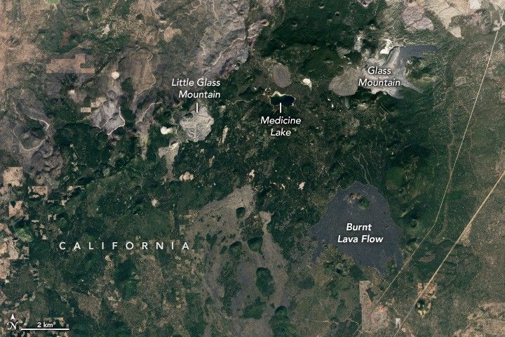 A mostly green region of California in interrupted by a black bit of land labeled burnt lava flow. Directly above that with some foliage between is a gray area labeled Glass Mountain. To the left of glass mountain is more foliage and another gray area labelled Little Glass Mountain. Medicine lake also sits equidistant between the two mountains.