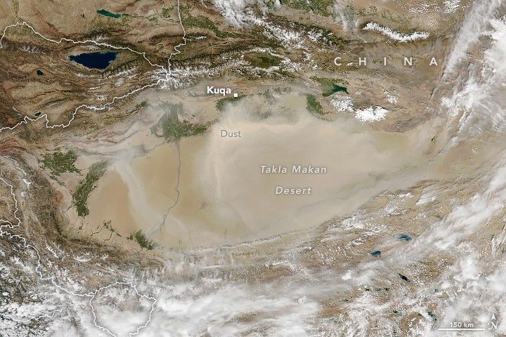 An oblong light and smooth beige region is labeled the Takla Makan Desert. Mountainous regions surround the area top and bottom, the bottom is mostly cloud covered and the upper mountains are tan in color with some green foliage sporadically located amid the peaks and valleys. Kuqa is labeled at the center of the upper region. The entire Desert and somewhat to the upper region, dust partially obscures.
