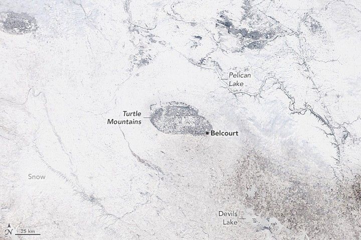 A completely white image with some oblong discoloration in the upper left and in the center. The center spot is labeled Turtle Mountains, and on the edge is an area known as and labeled Belcourt. Devils Lake is labeled in the lower right and Pelican Lake is labeled directly above Belcourt in the image.